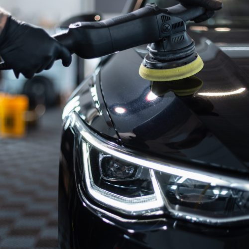 Professional man with polishing tool polishing black car in garage . Detailing. Varnish care and scratch removal
